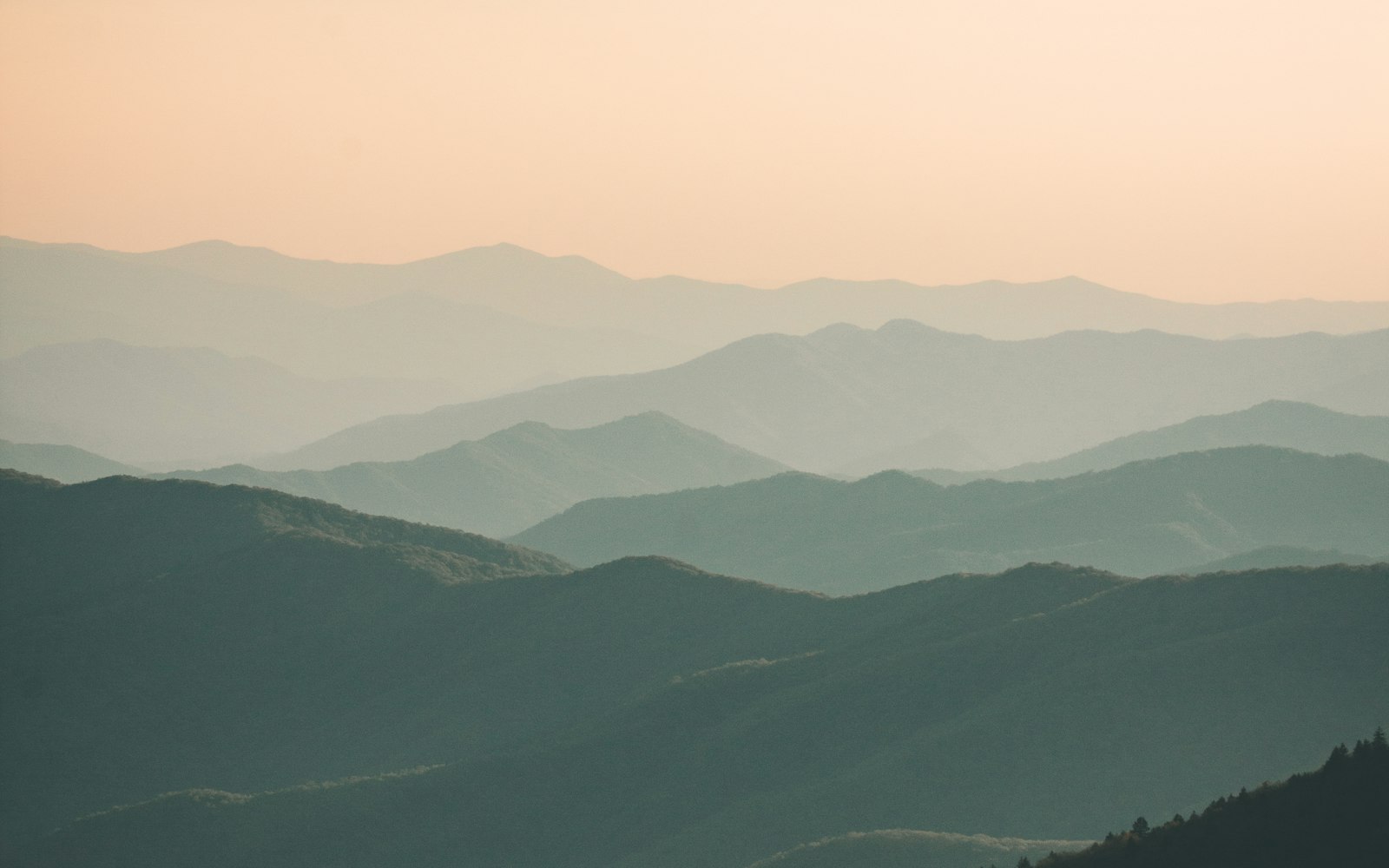 Layered mountain ridges fading into a pale sunset sky