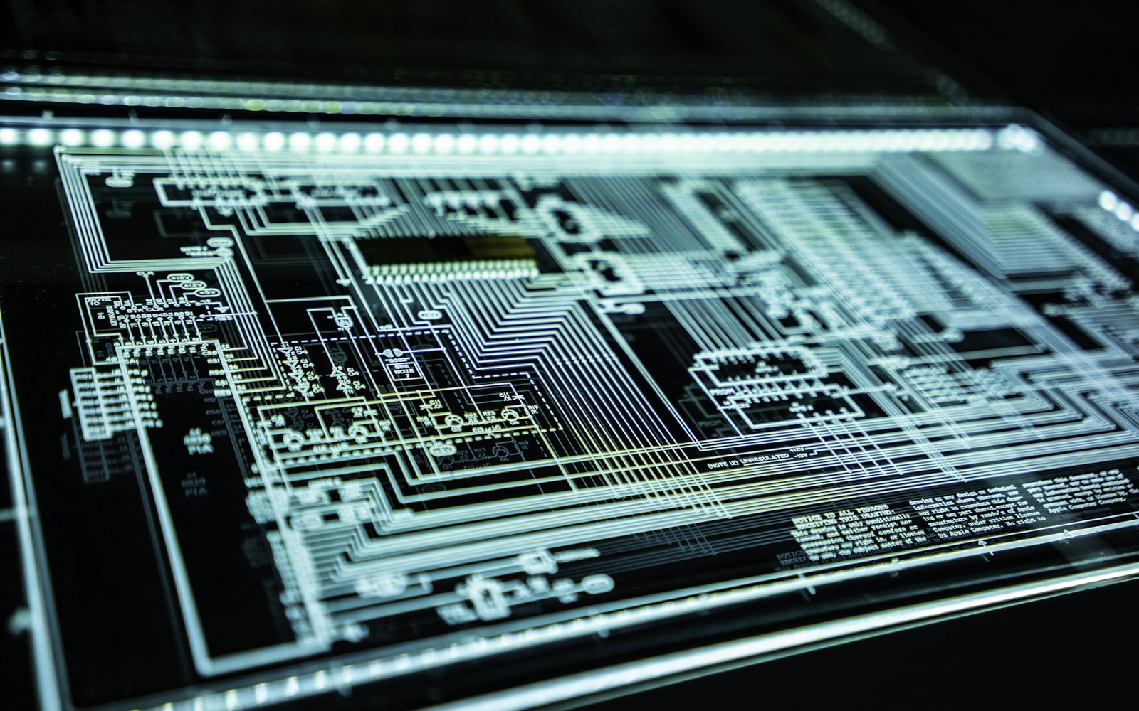 A dark circuit board illuminated with blue-green light