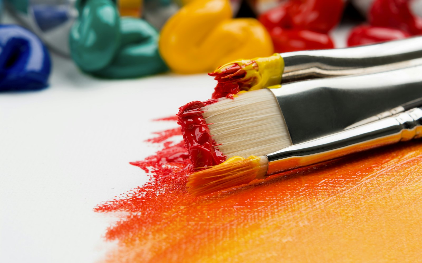 A paintbrush spreading bright red paint across a surface