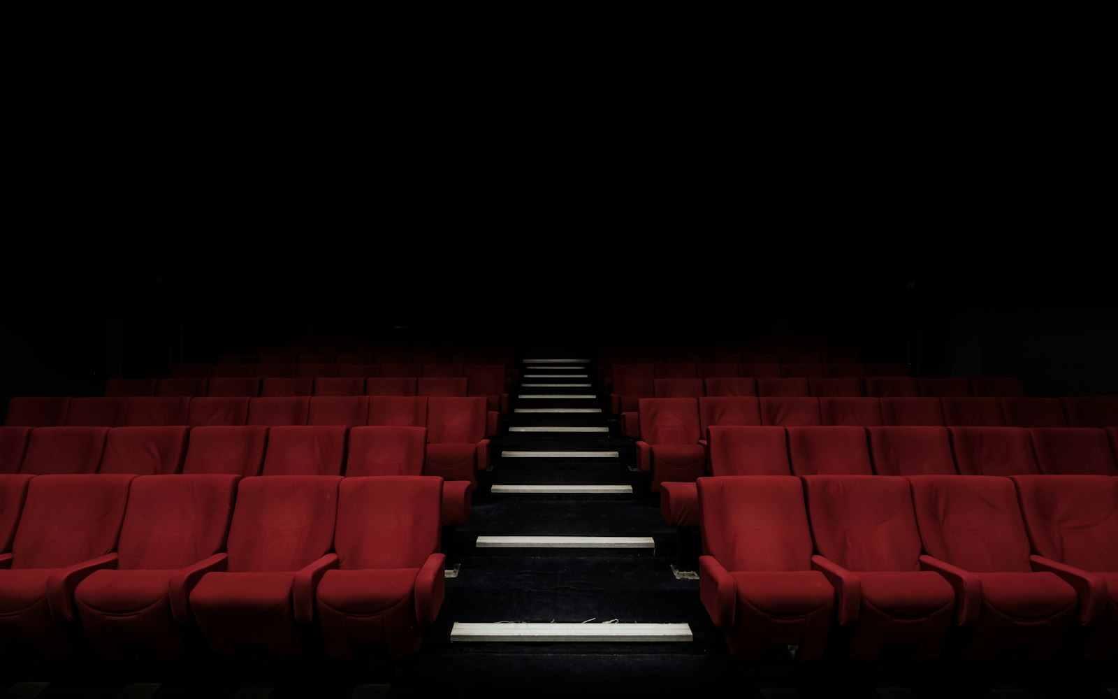 Empty red cinema seats facing a dark screen