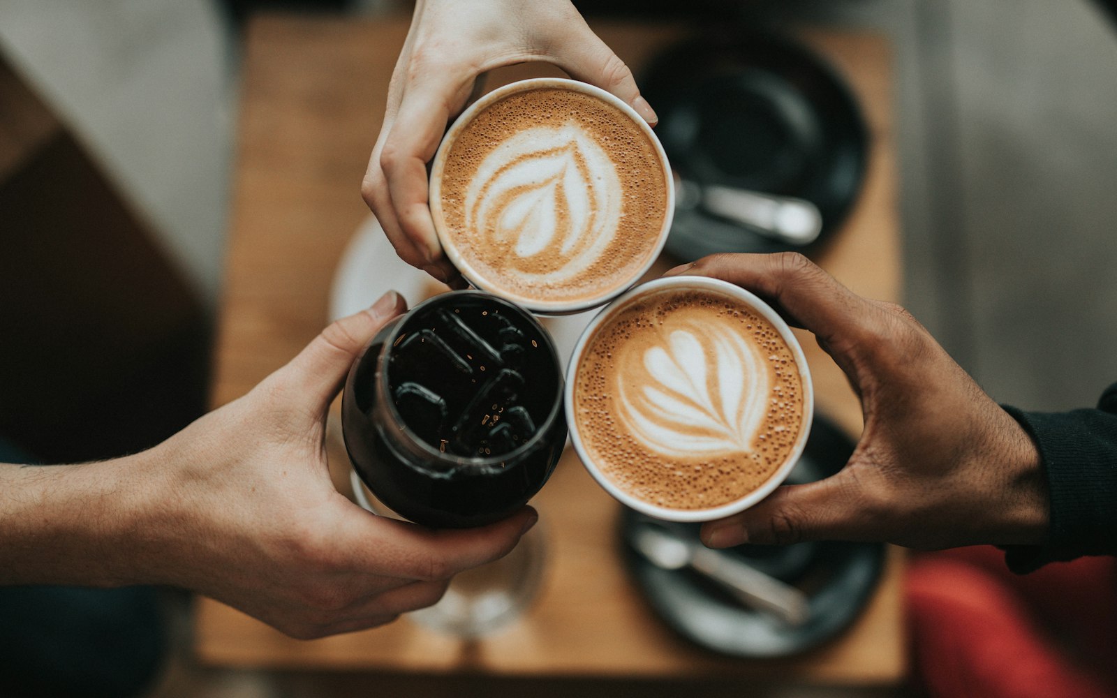 Three hands holding cups of latte coffee