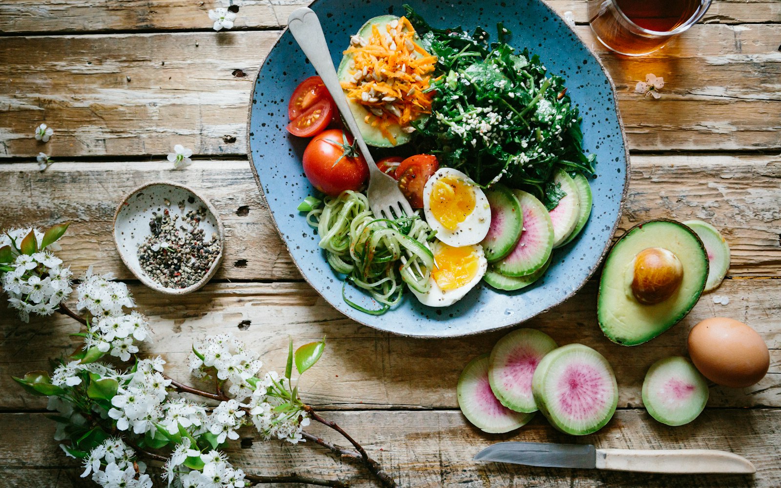 A colorful salad bowl beside fresh flowers on a wooden table
