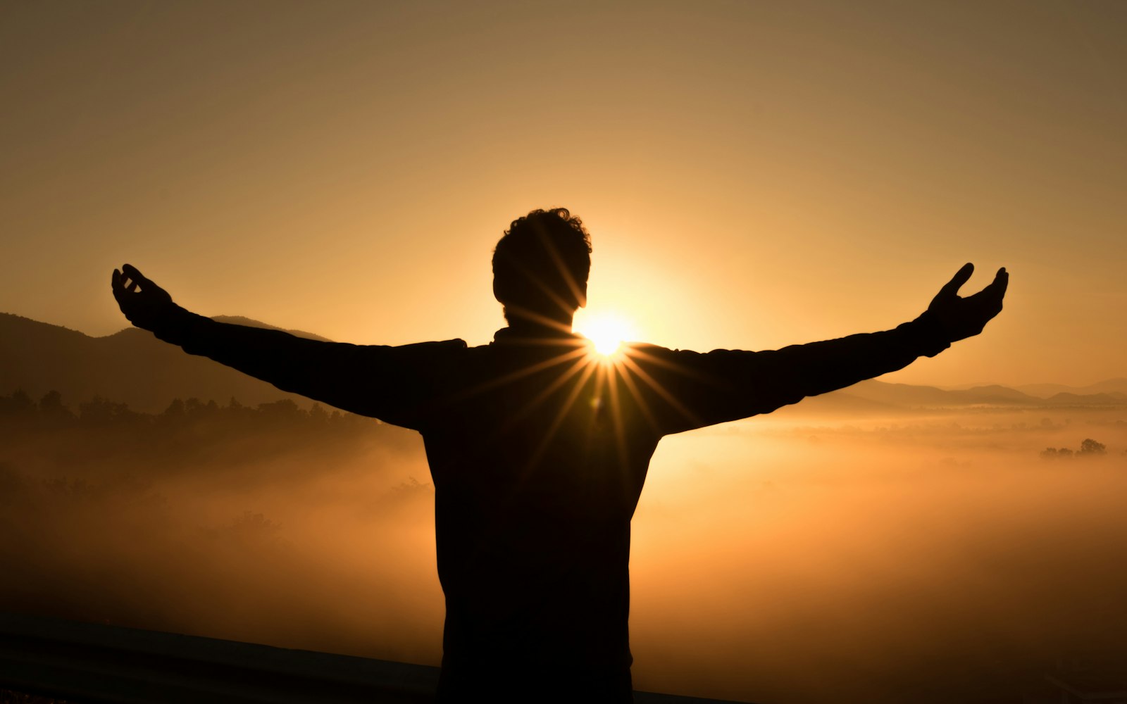 A person standing with arms open toward a sunrise