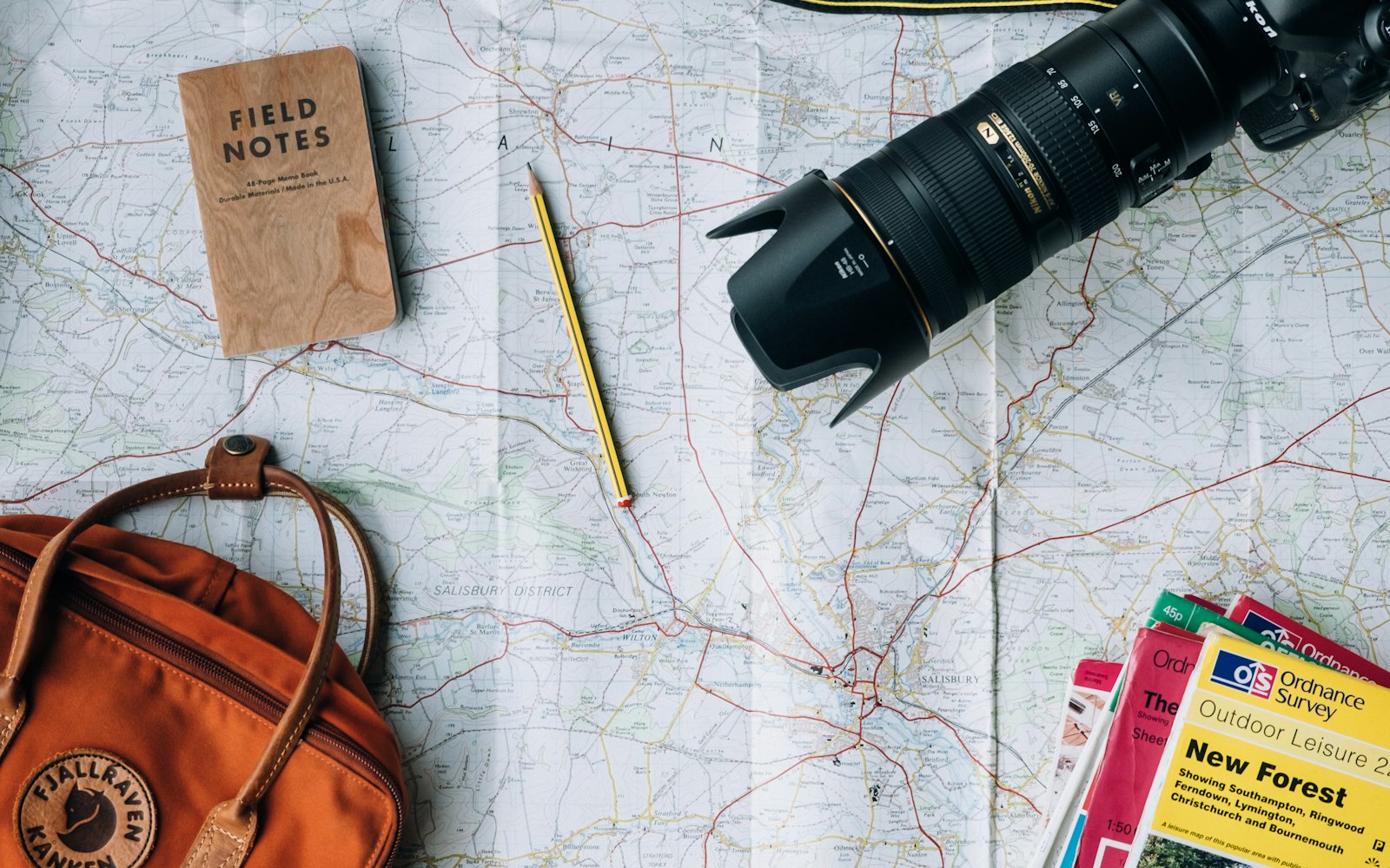 A notebook, camera, phone, and travel items arranged on a table